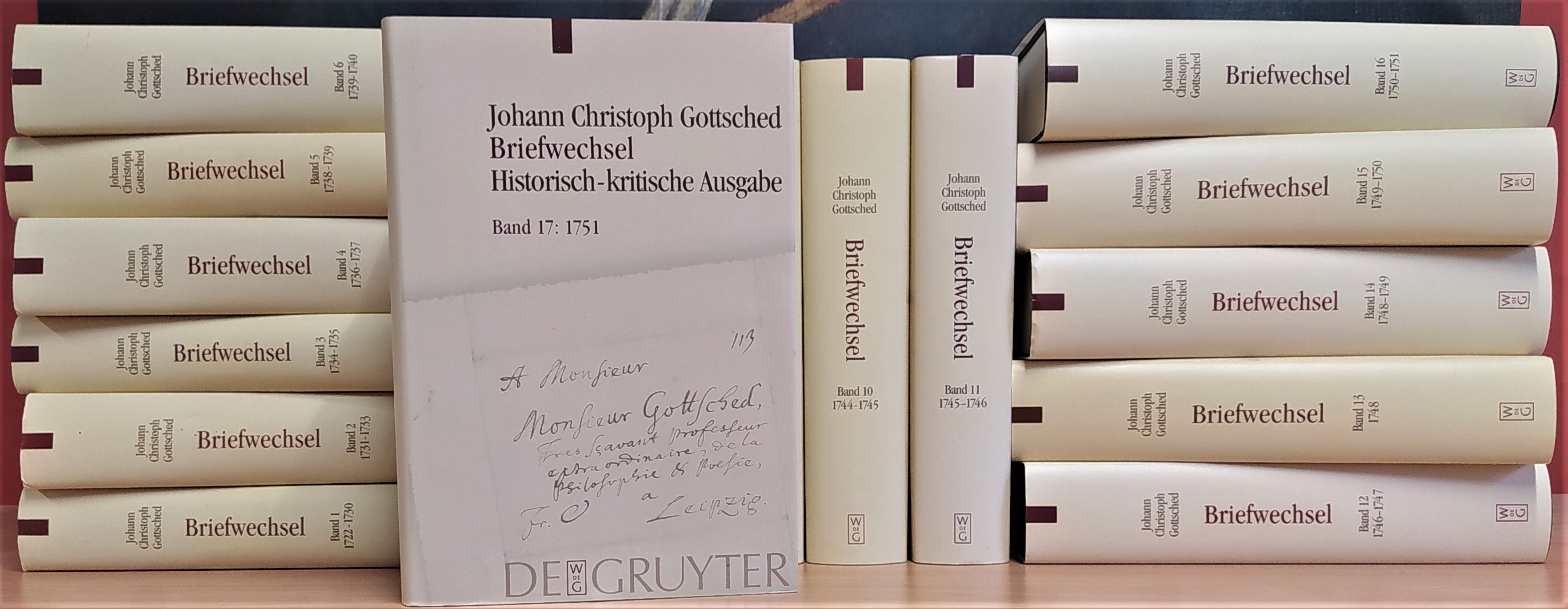 Gestapelte Bücher, liegend und stehend. Auf den Buchrücken erkennt man das Wort "Briefwechsel", auf einem frontal stehenden Buch steht: "Johann Christoph Gottsched. Briefwechel. Historisch-kritische Ausgabe. Band 17: 1751. De Gruyter".