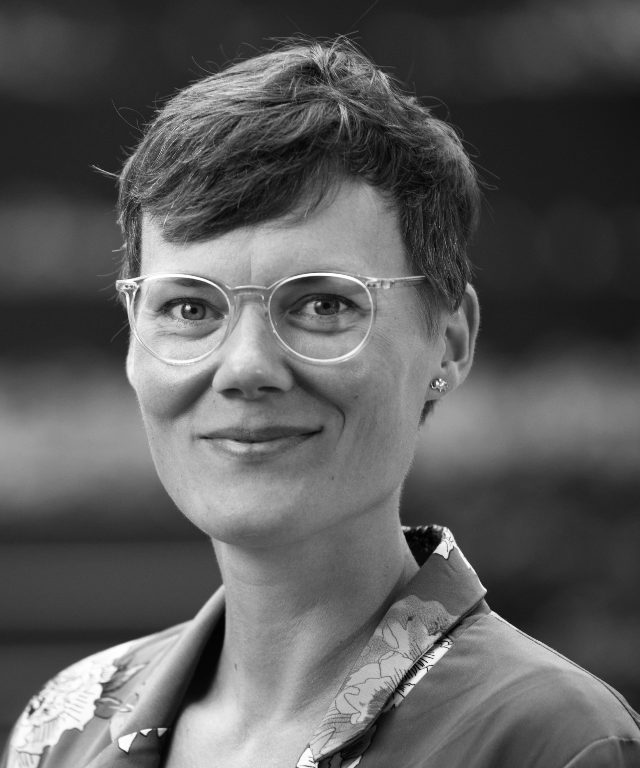 Schwarz-weiß-Porträtfoto einer lächelnden weiblichen Person mit Brille, im unteren Bildrand ist ein grünes Grafikelement mit der Aufschrift Junges Forum