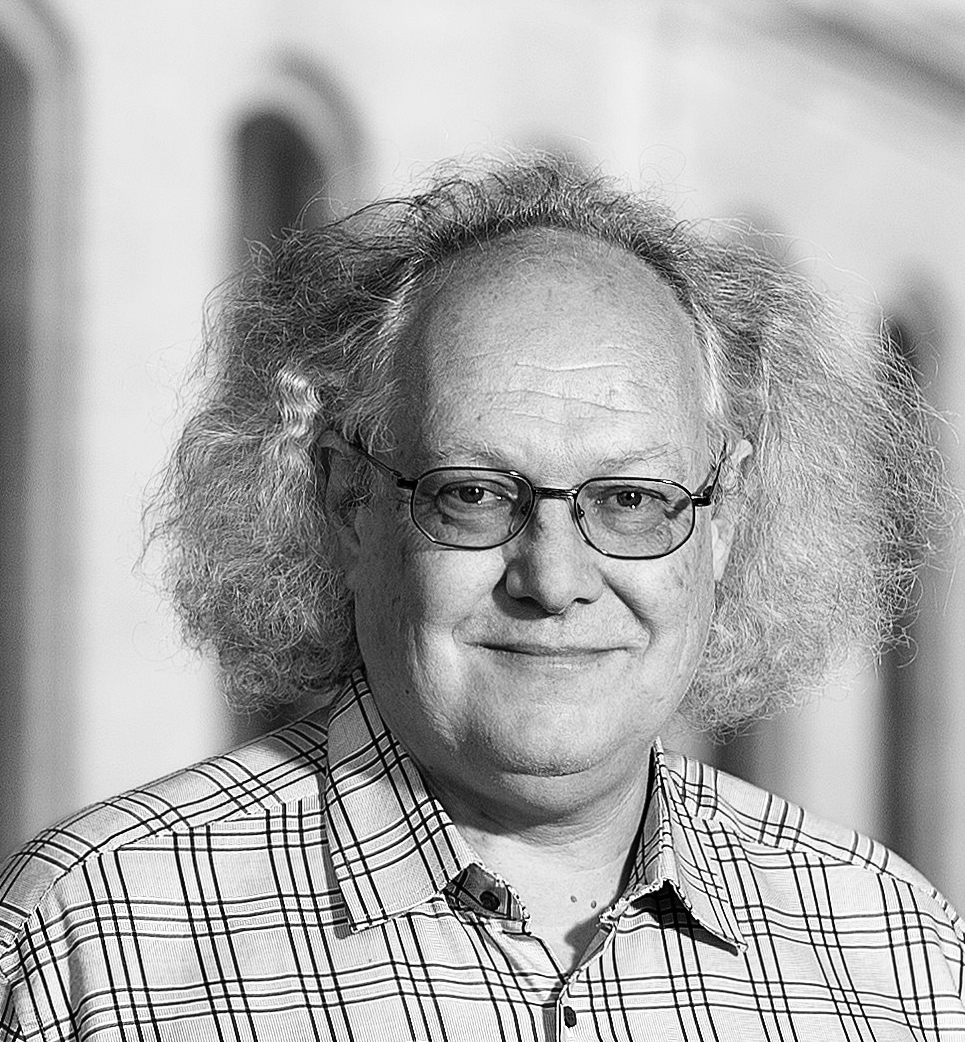 Schwarz-weiß-Porträtfoto einer lächelnden männlichen Person mit Brille und kariertem Hemd